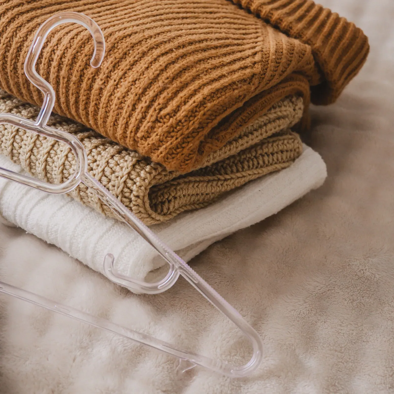 Folded knit sweaters in camel, oatmeal and cream with a clear hanger