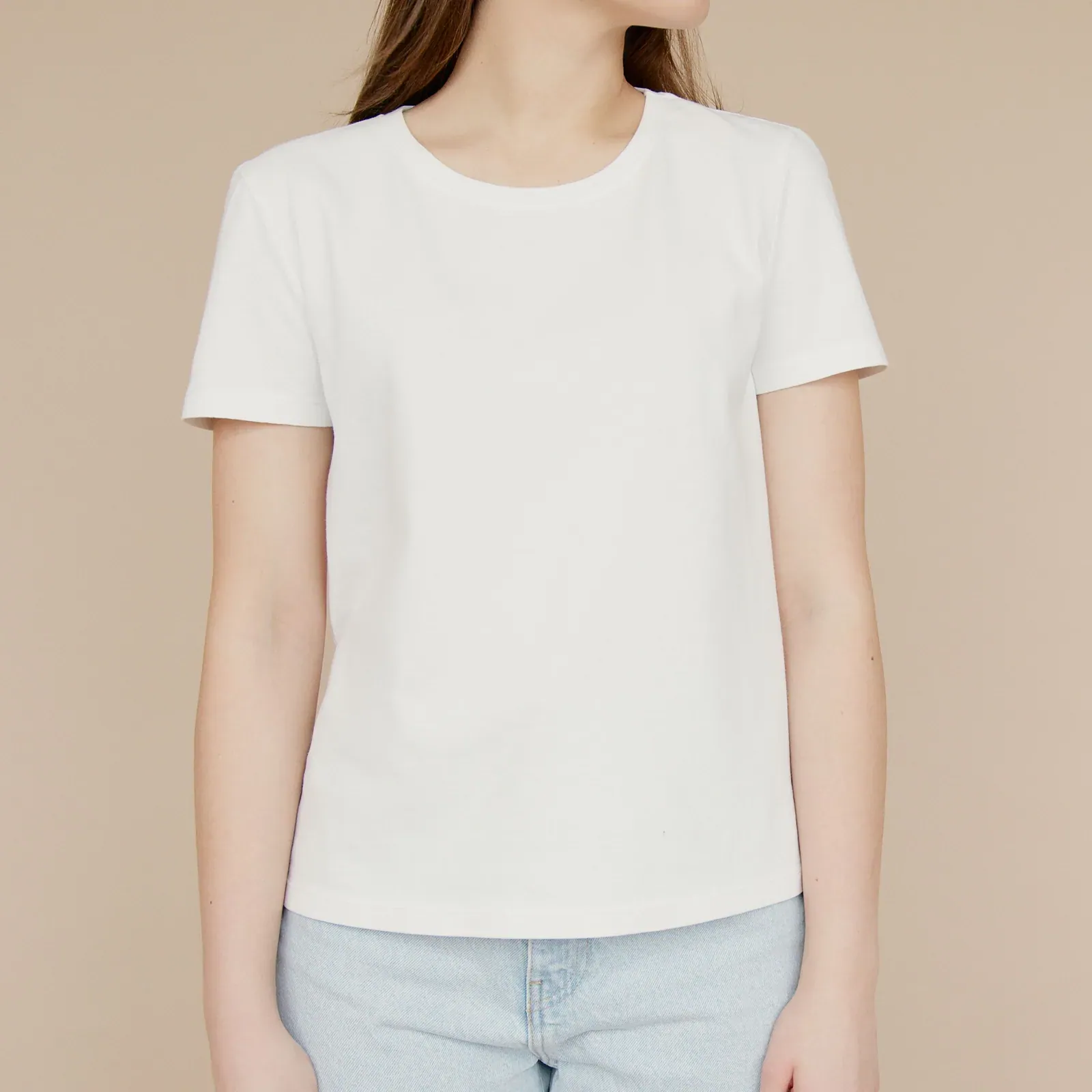 White crew-neck T-shirt worn with light jeans against a beige wall