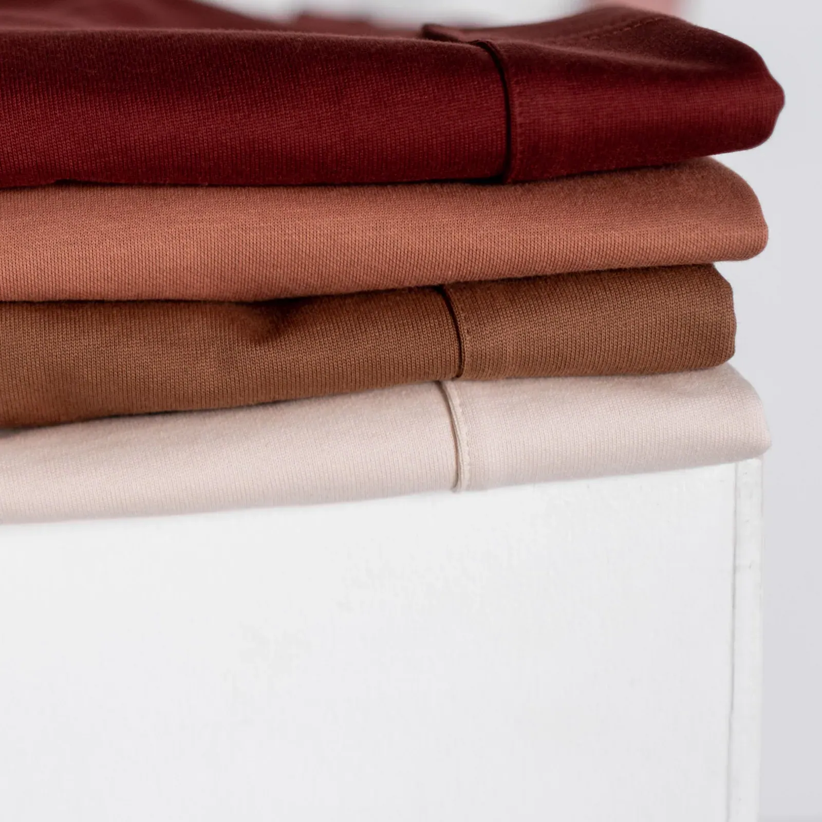Stack of folded T-shirts in burgundy, rust, tan and cream