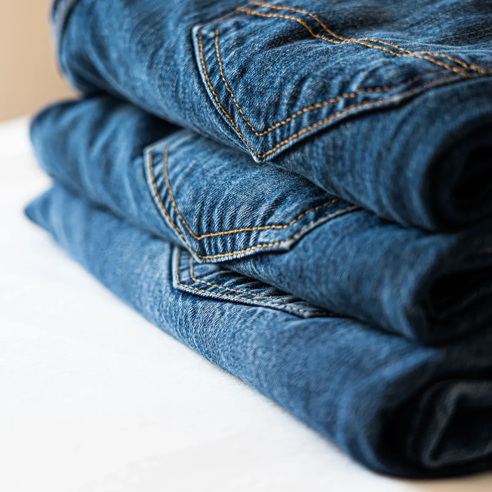 Stack of folded blue jeans on a white surface
