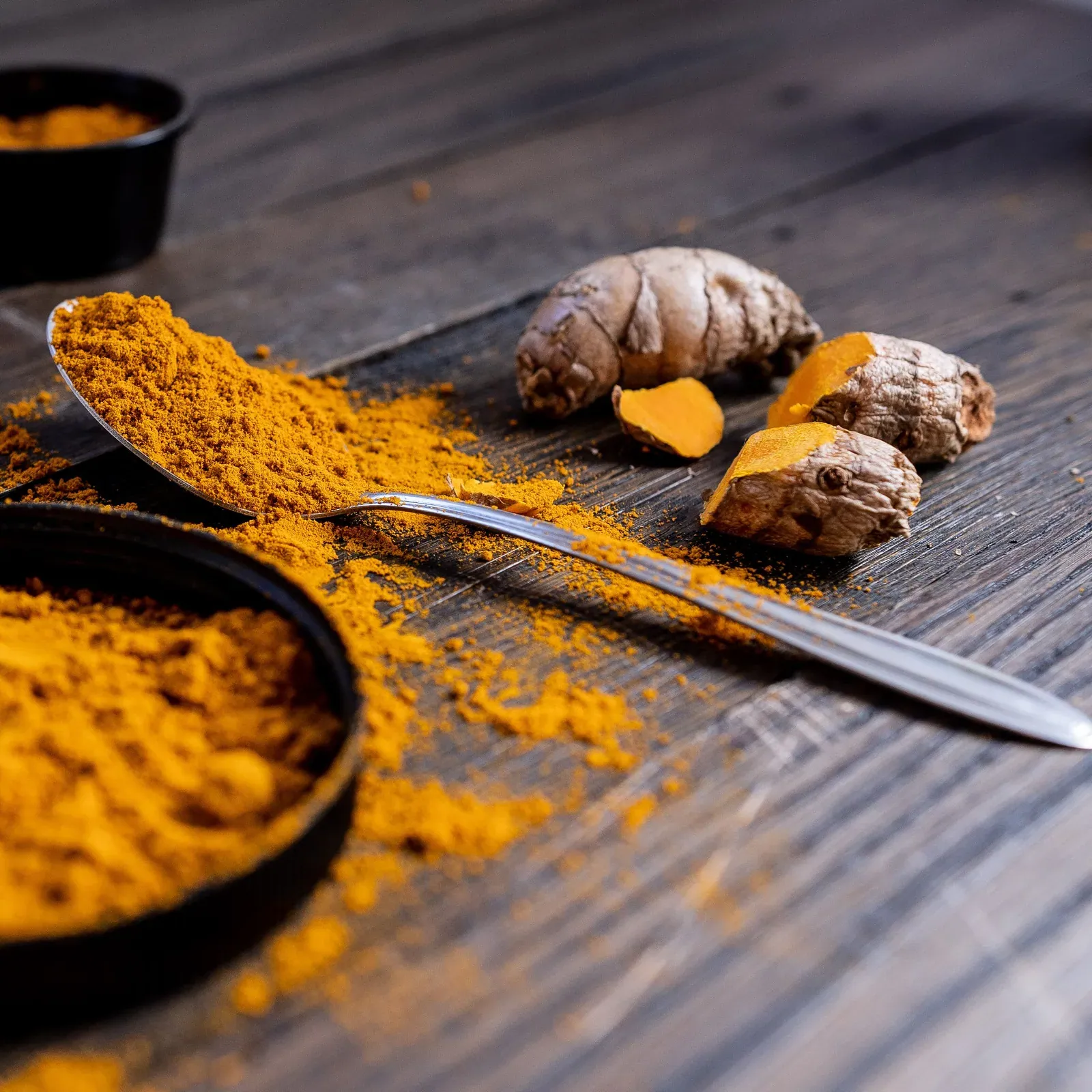 Turmeric powder and fresh turmeric root on dark wood