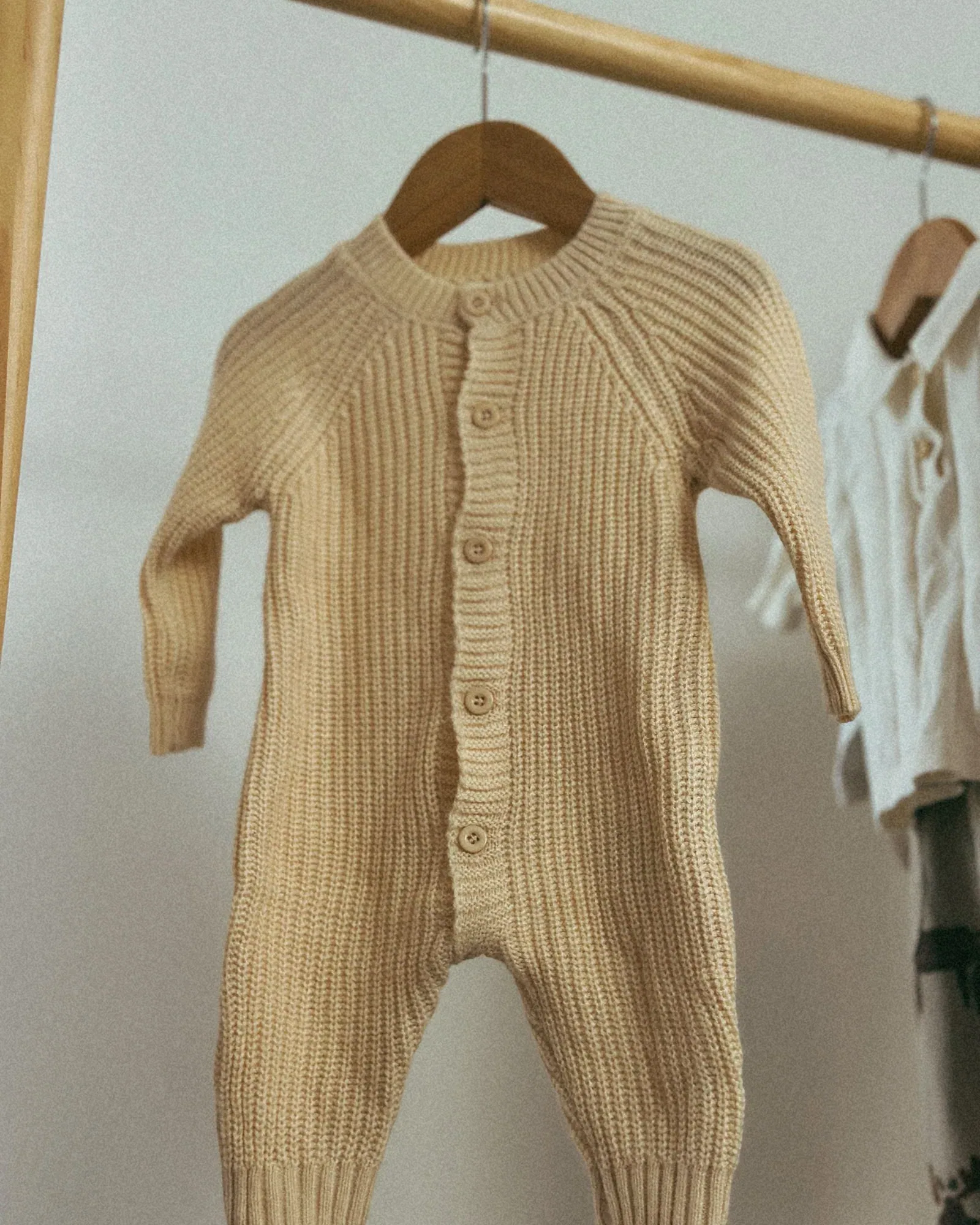 Oatmeal knitted baby romper on a wooden hanger