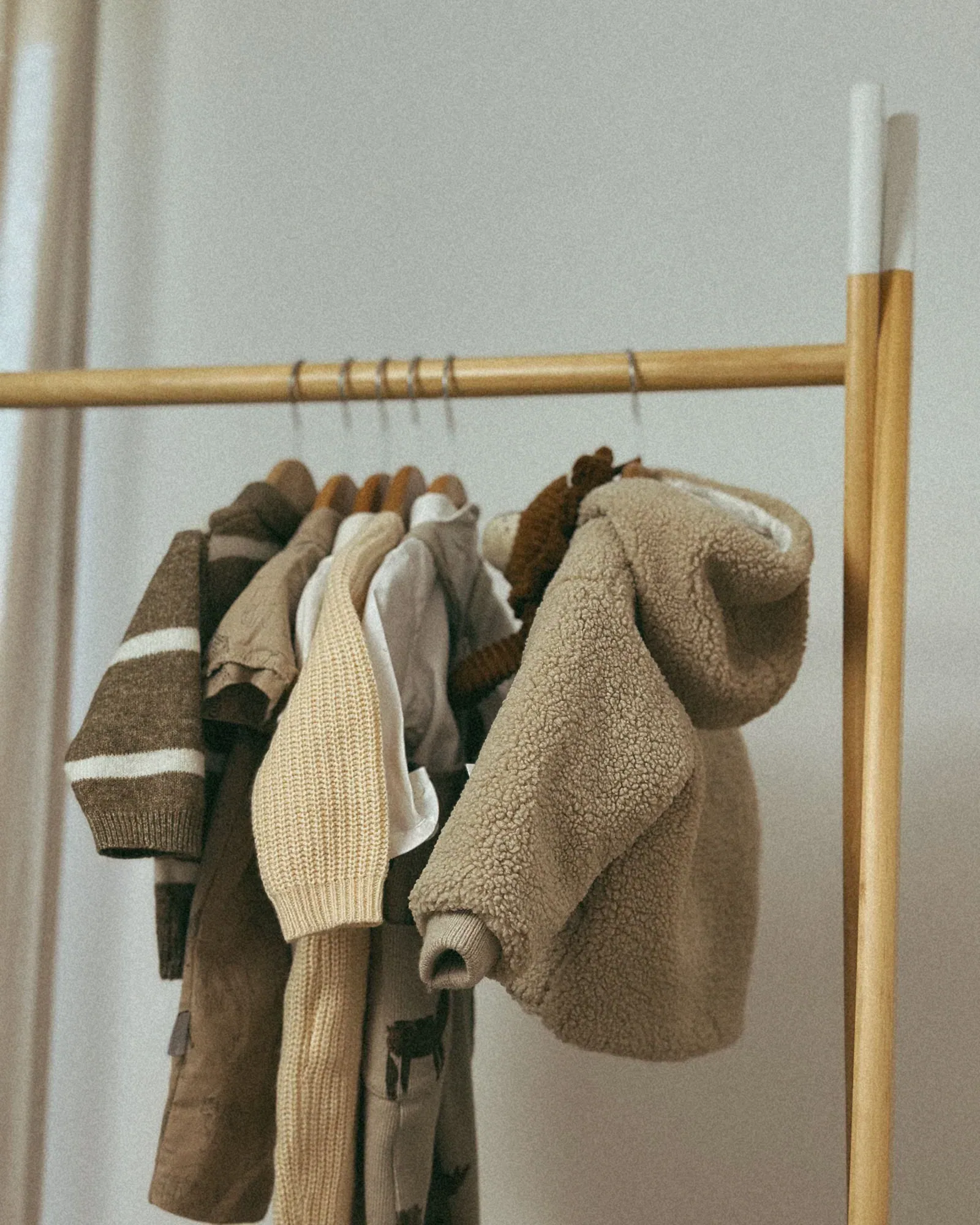 Children's jackets and knits in brown and beige on a wooden rail
