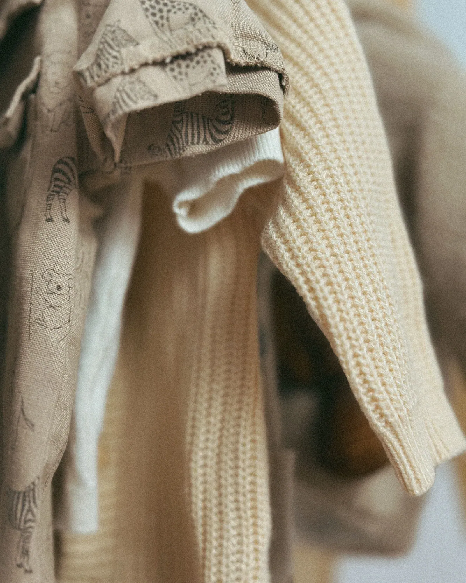 Children's beige knit cardigan and an animal-print top on a rail, close-up