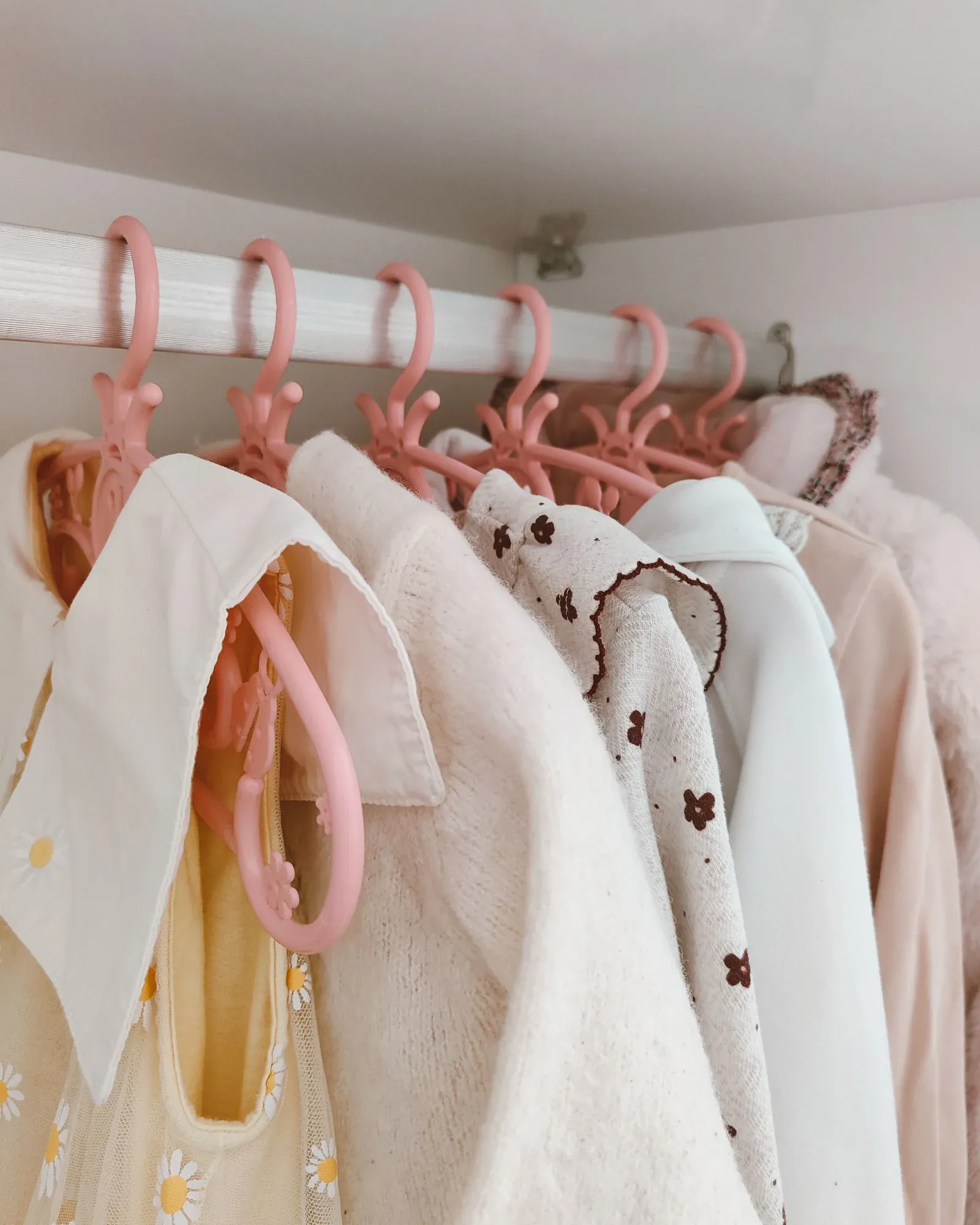Children's shirts, cardigans and dresses in cream and white on small pink hangers