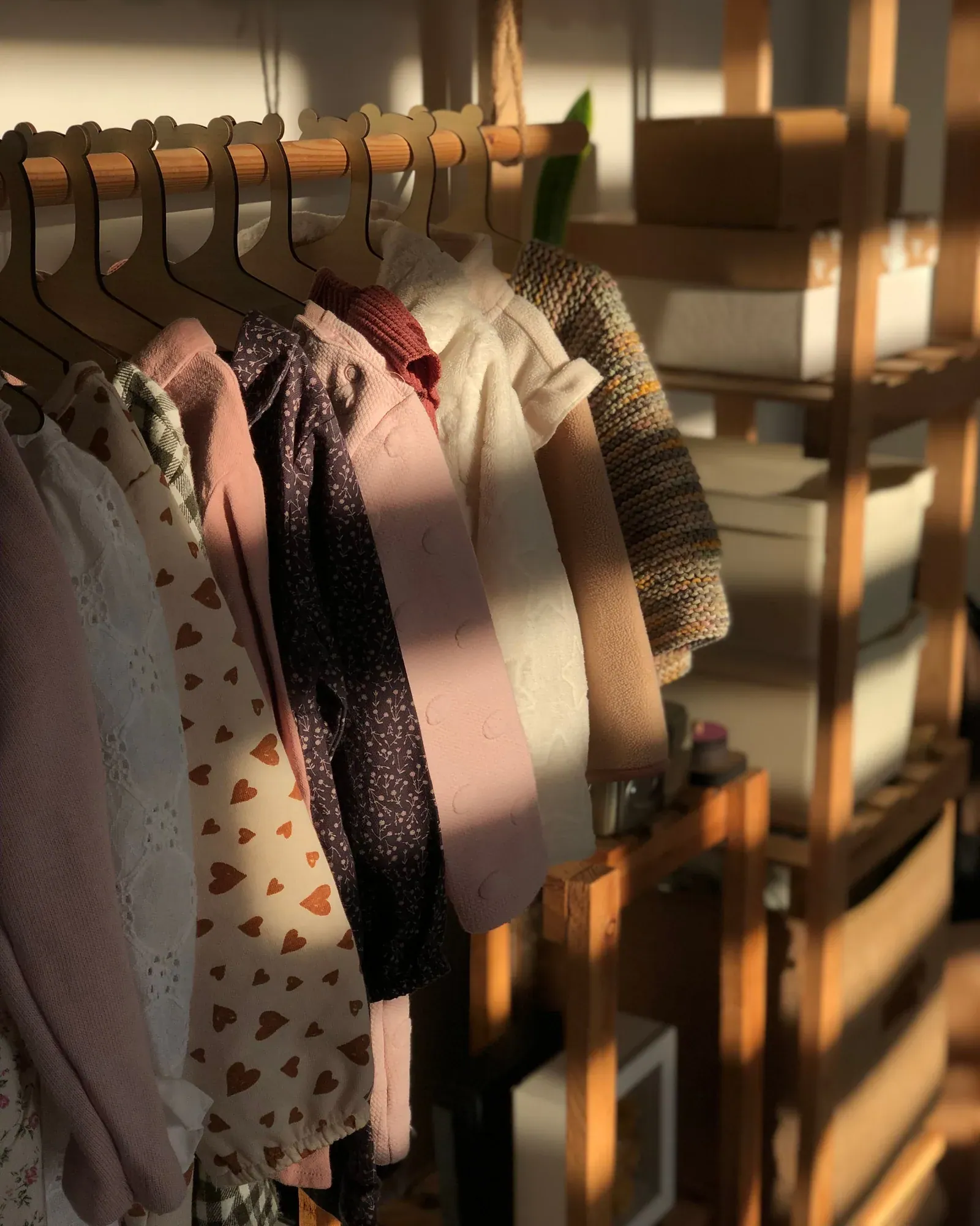Children's dresses and knits in blush, cream and brown on a wooden rail