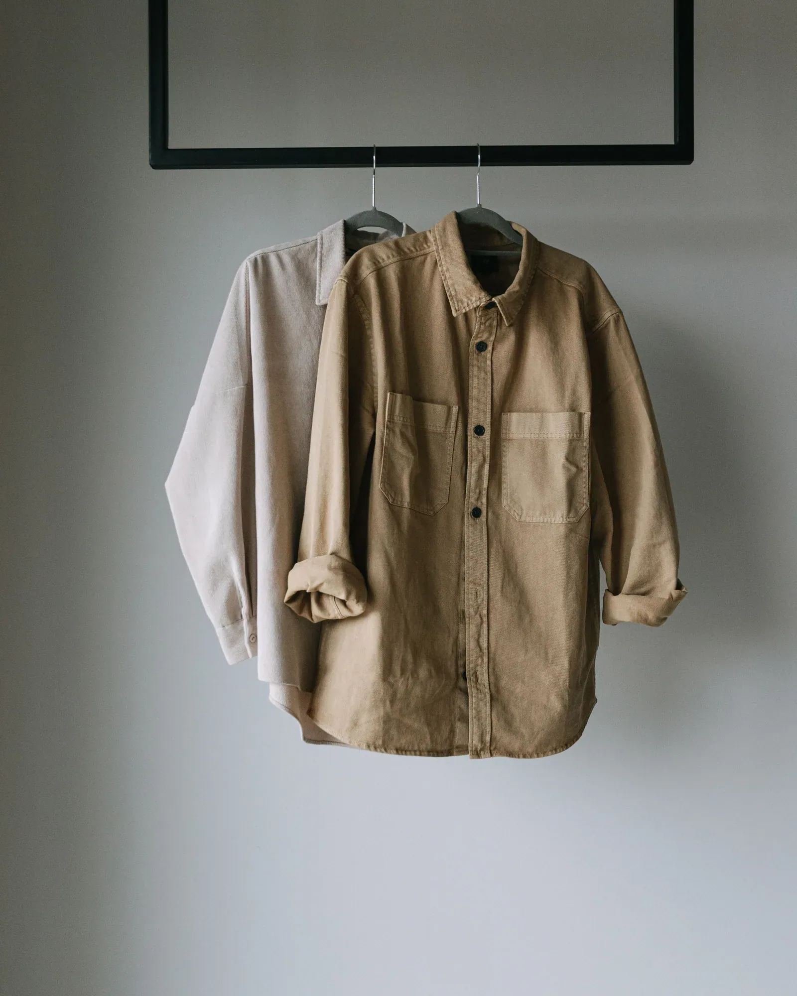 Two button-down shirts in stone and khaki on a hanger