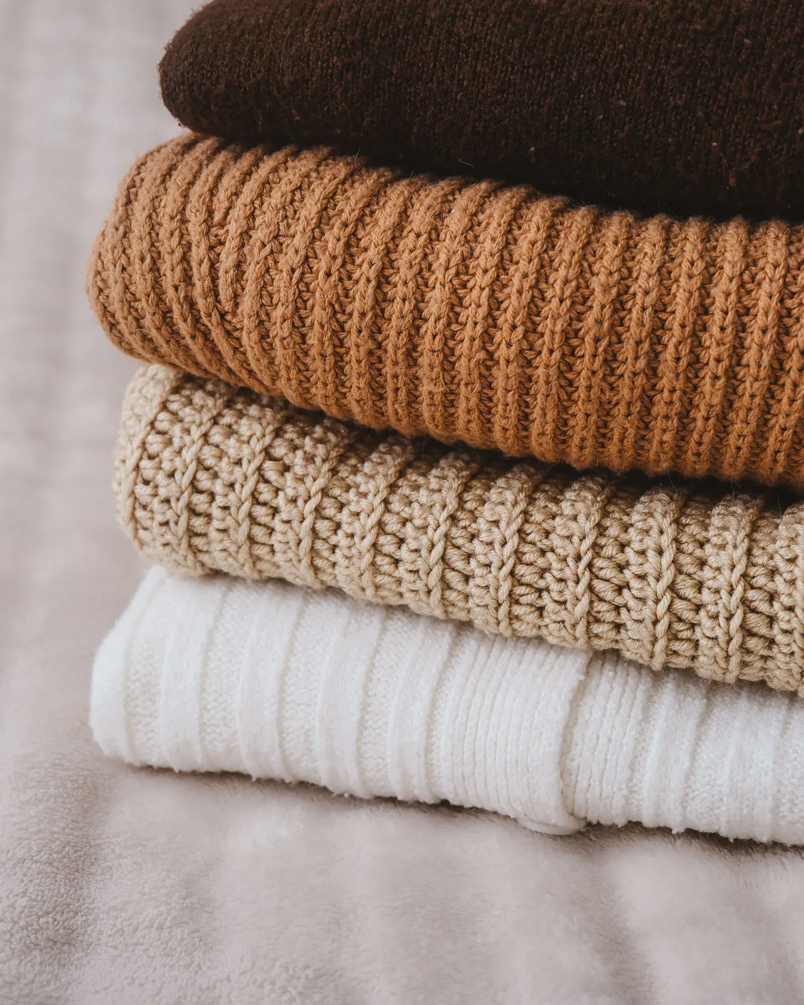 Stack of folded knit sweaters in brown, rust, oatmeal and white
