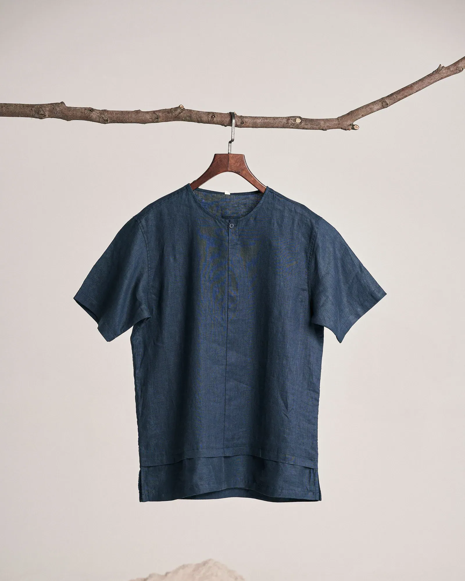 Navy short-sleeved shirt on a wooden hanger hung from a branch