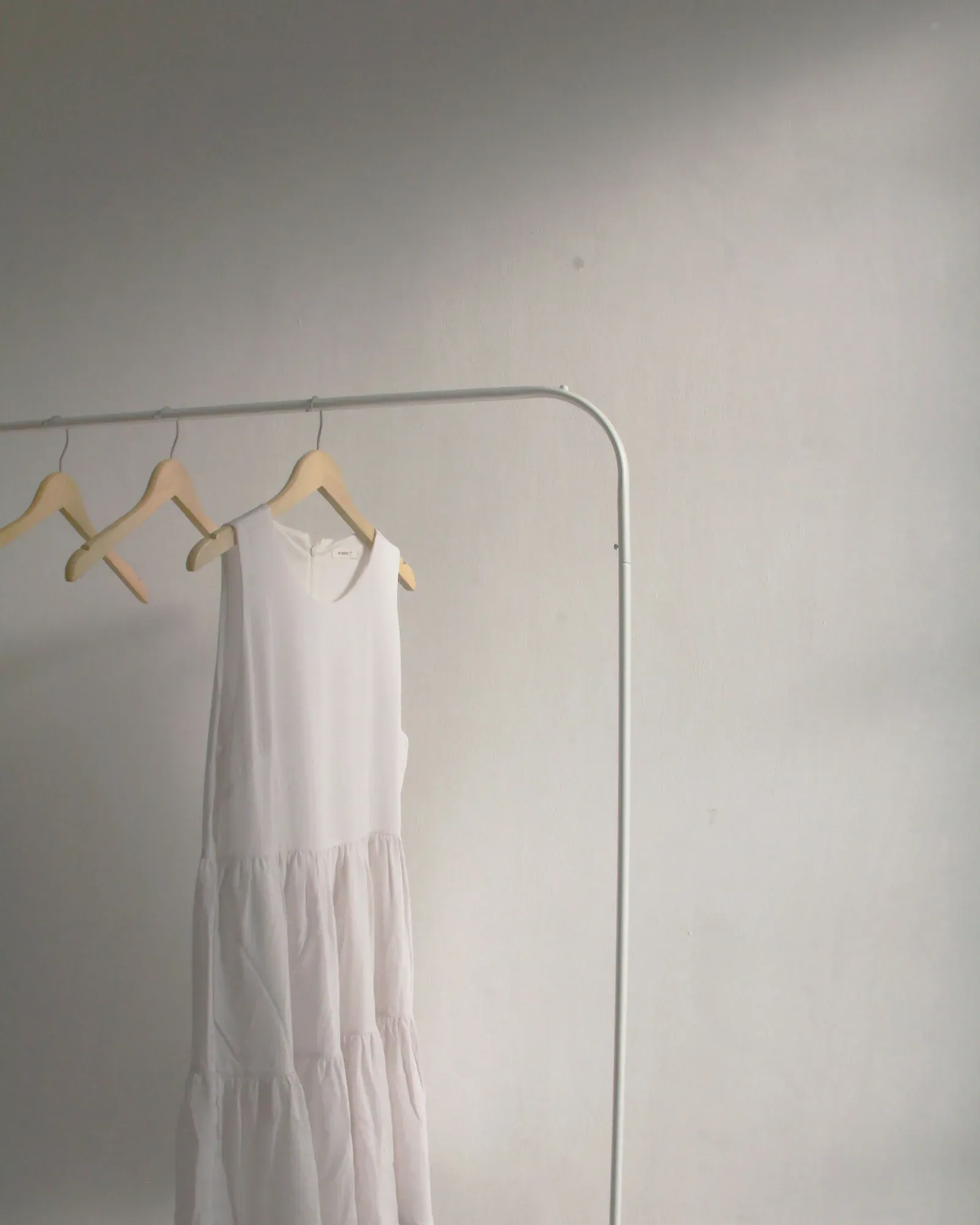 White sleeveless dress on a clothes rail against a grey wall
