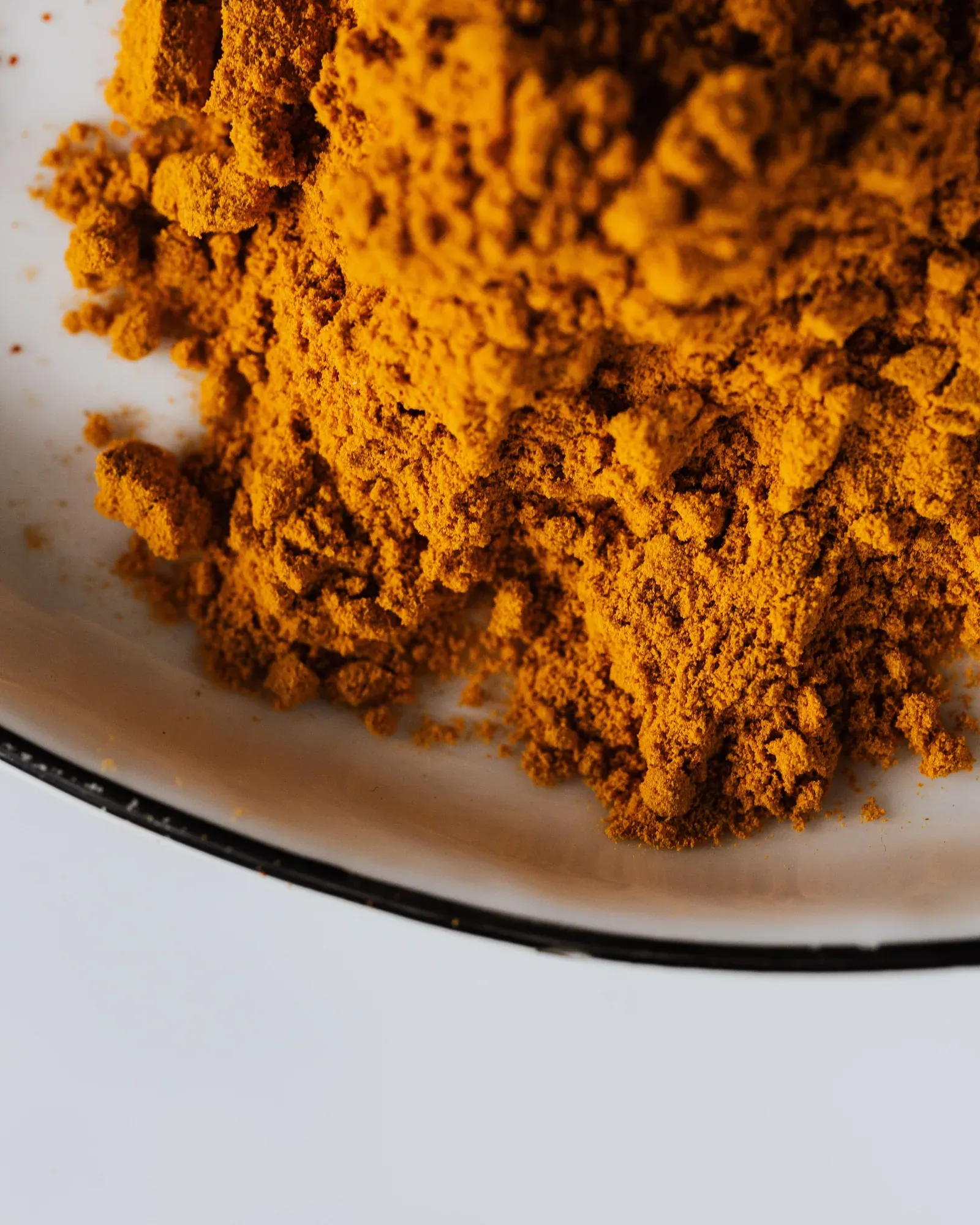 A heap of ground turmeric in a white enamel bowl