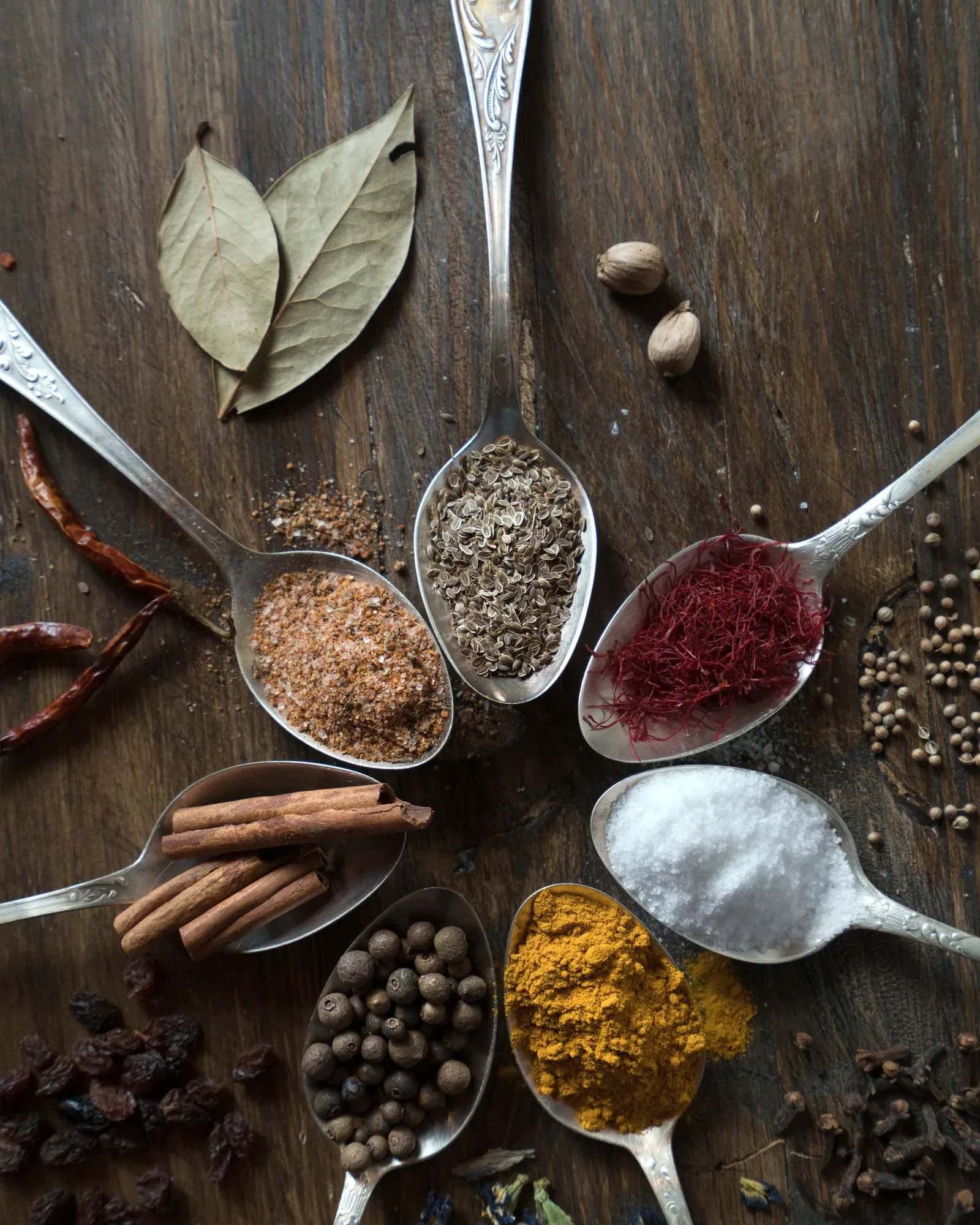 Ground and whole spices in spoons arranged in a circle on dark wood