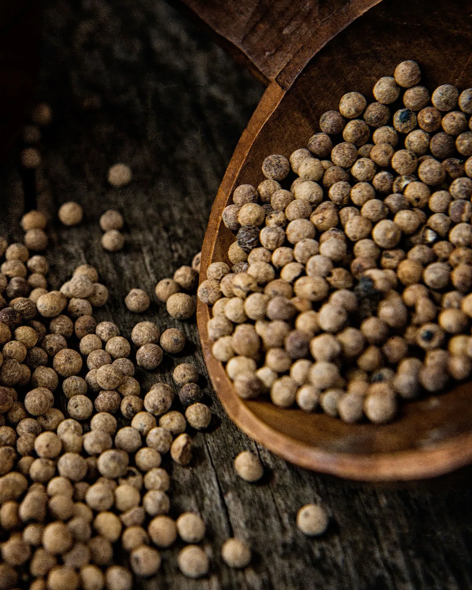 Small round whole spices spilling from a wooden bowl