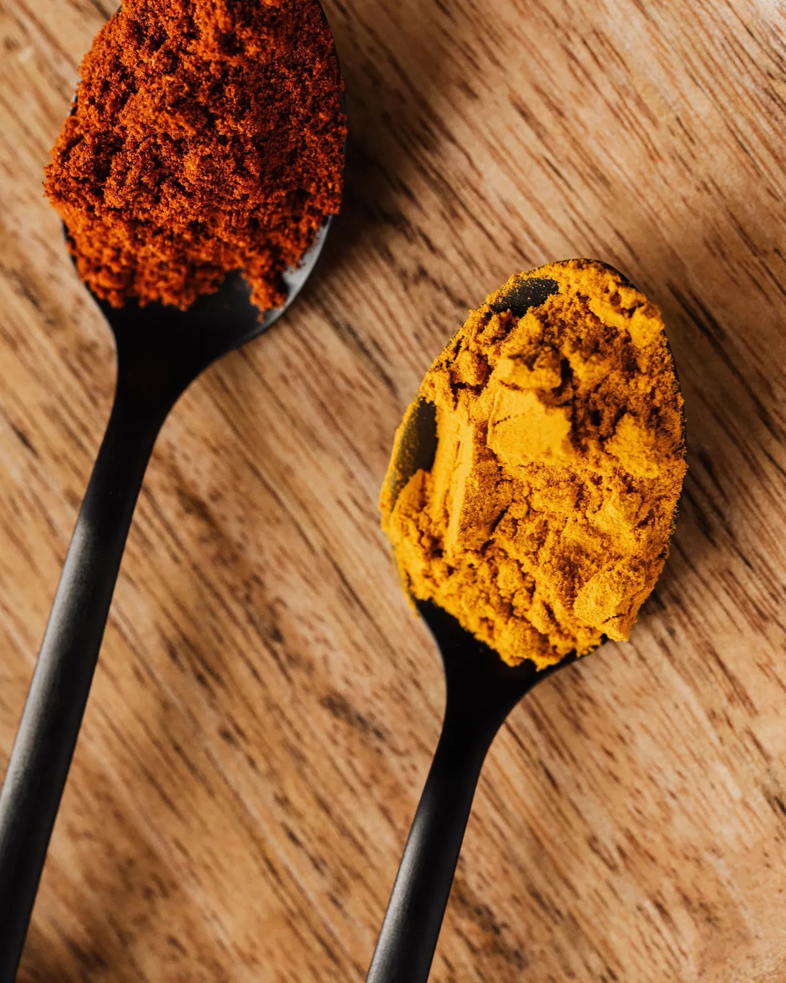 Two spoons of ground paprika and turmeric on a wooden board