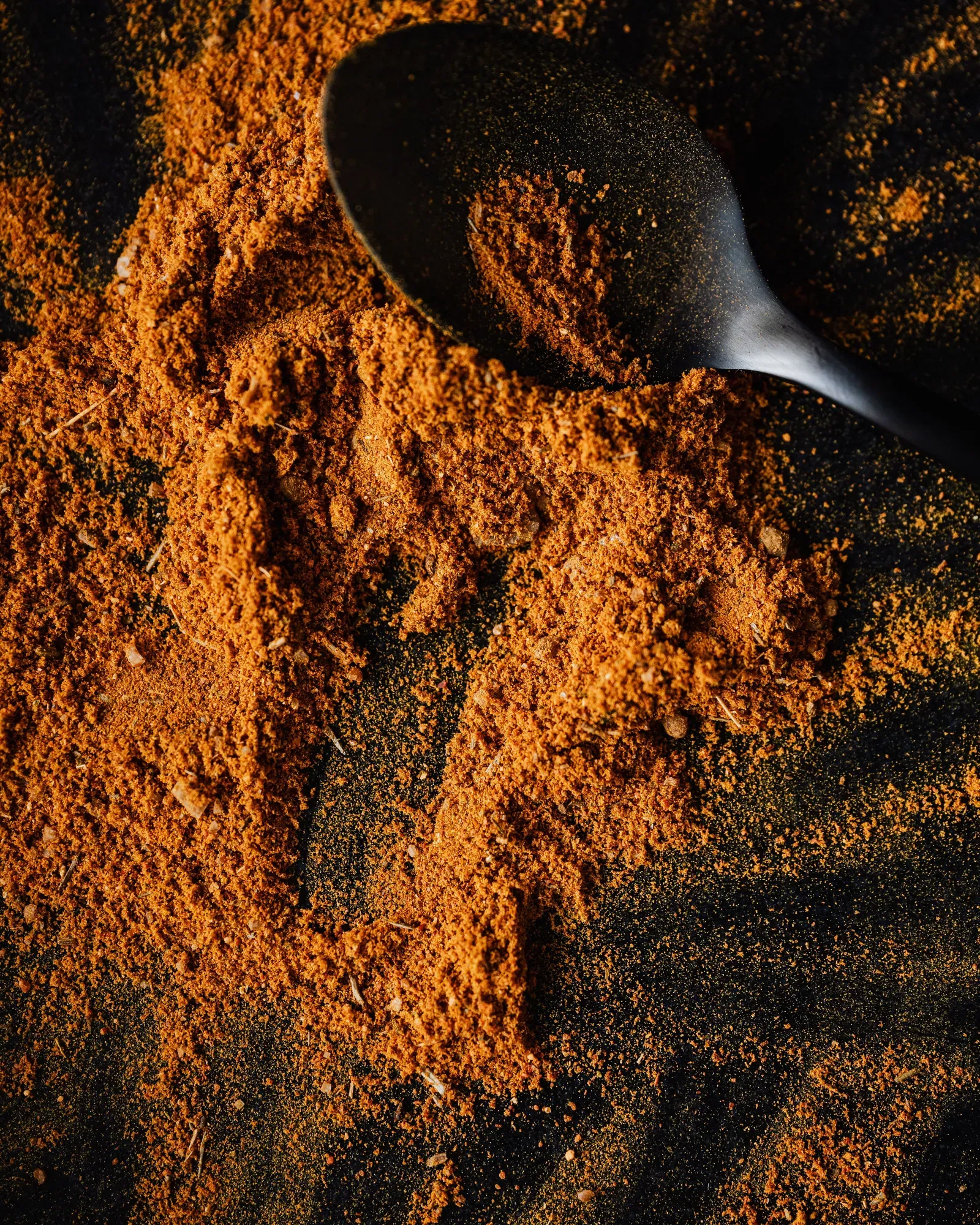 Ground spice heaped on a dark surface with a spoon